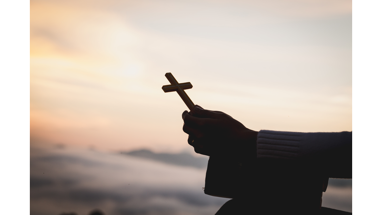 Silhouette Hand Holding Cross Against Sky During Sunset