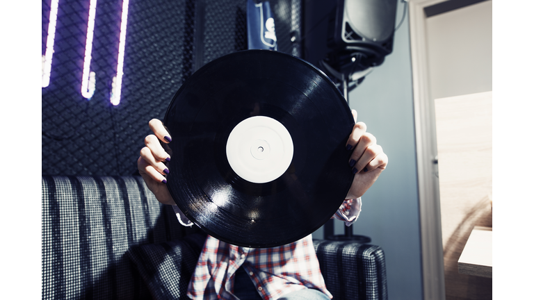 close up to young woman's hands holding a white label vinyl record in front of her