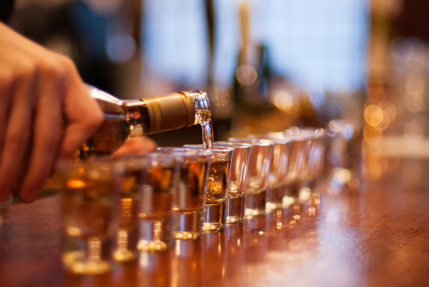 Person pouring a line of shots in a bar