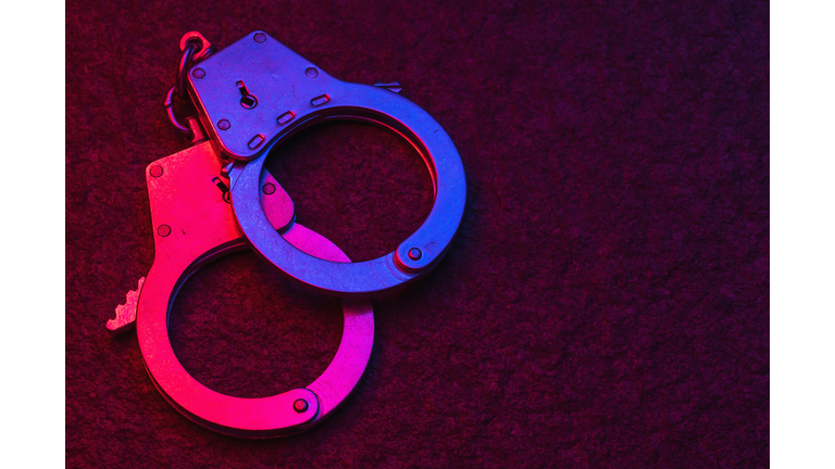 Handcuffs on dark background illuminated by flashing lights of police car with copy space