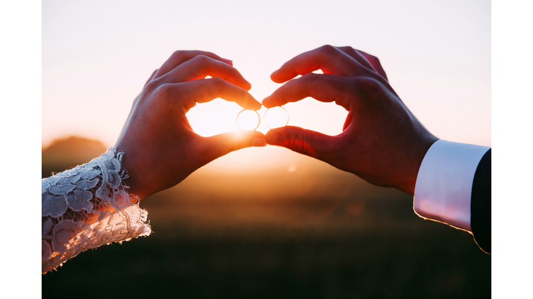 Two married people holding wedding rings at sunset.