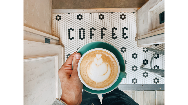 Man holding a cup of coffee above "COFFEE" word on the floor