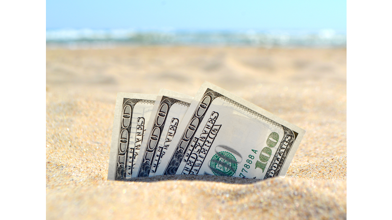 Money dolars half covered with sand lie on sandy beach near sea