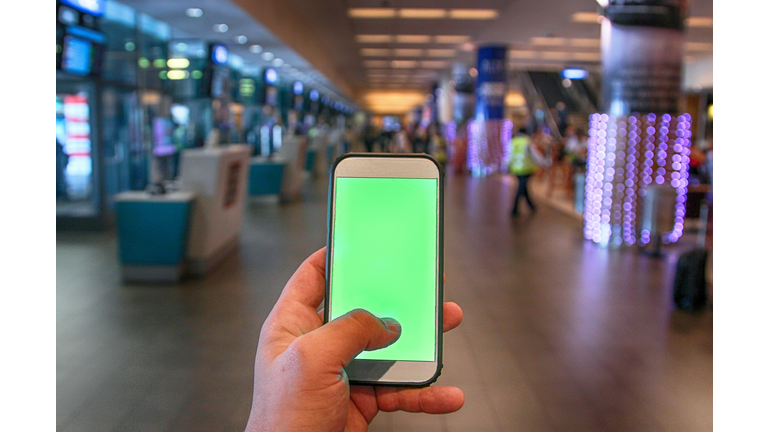 a Young man holding a green screen smartphone at Cape Town International Airport.