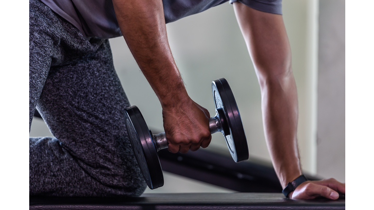 Closeup of handsome man doing bodybuilder exercises with dumbbell in ghym