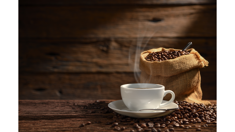 Cup of coffee with smoke and coffee beans on old wooden background