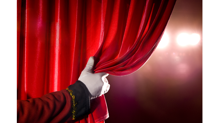 Usher opening red theater curtain, with spotlights