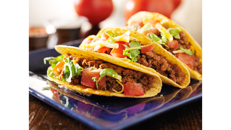 three beef tacos with cheese, lettuce and tomatoes