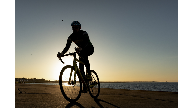 Cyclist on path by sea at sunset
