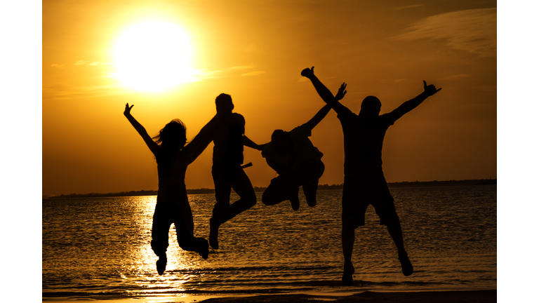 Spring break backlit group of young people jumping on beach