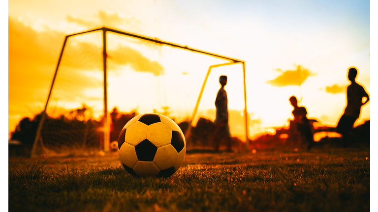 An action sport picture of a group of kid playing soccer football for exercise in before the sunset.