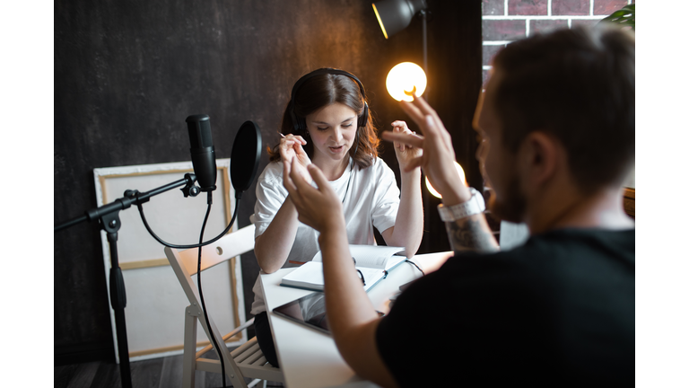 Young woman interviewing a guest in studio for podcast.