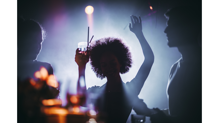 Silhouette of a girl with an afro dancing with a cocktail in her hand in a night club