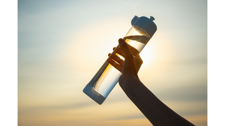 Human hand holds a water bottle against the setting sun.