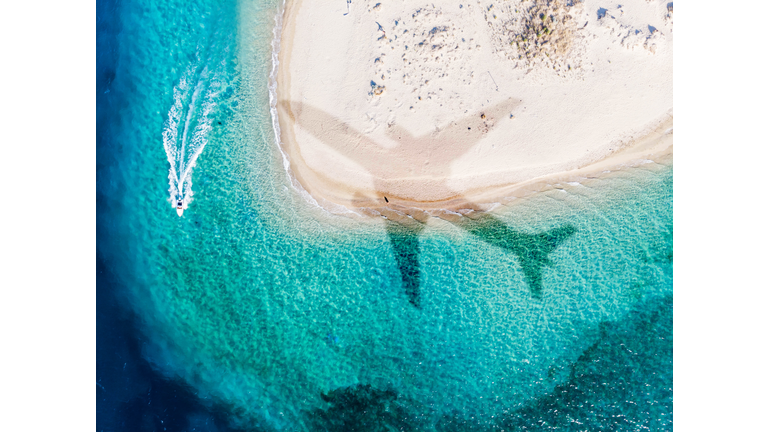 Airplane shadow flying above paradise beach taking from window.