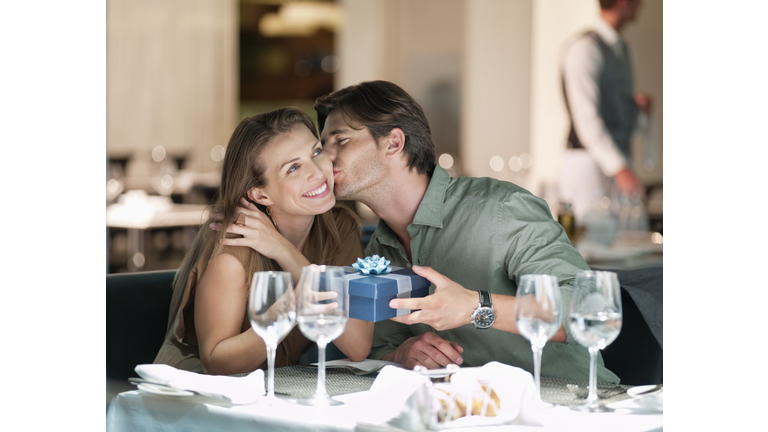 Man kissing and giving gift to woman in restaurant