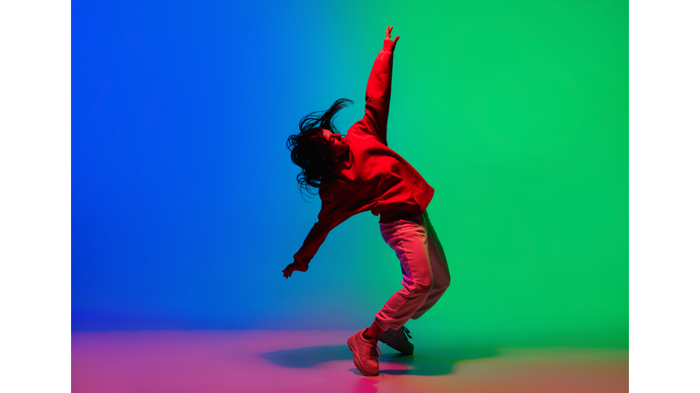 Stylish sportive girl dancing hip-hop in stylish clothes on colorful background at dance hall in neon light. Youth culture, movement, style and fashion, action.