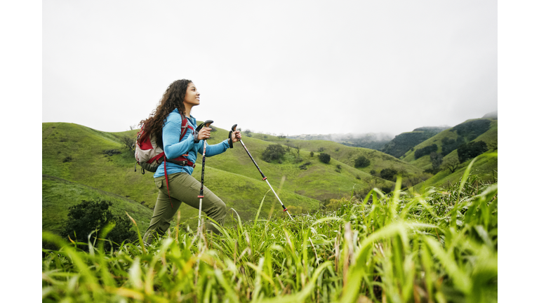 Smiling mixed race woman hiking with walking sticks