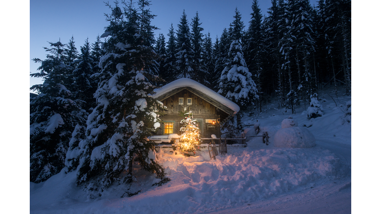 Austria, Altenmarkt-Zauchensee, sledges, snowman and Christmas tree at illuminated wooden house in snow at night