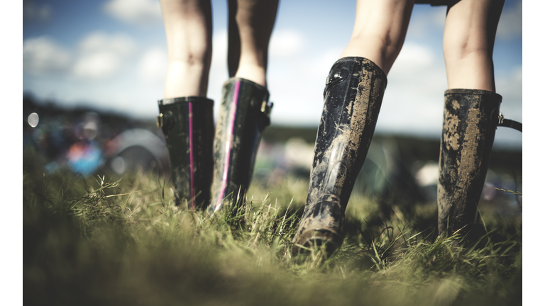 Low section rear view of two young women at a summer music festival wearing muddy Wellington boots.