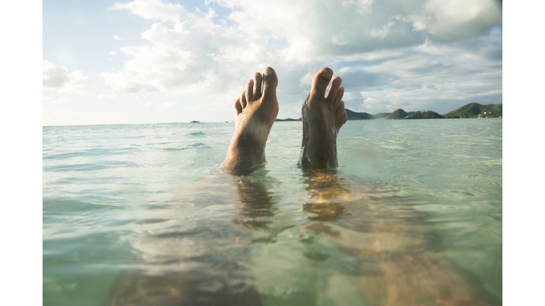 POV Man floats in tropical sea, feet out of water