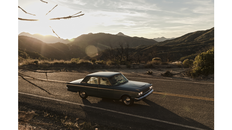 Young man driving vintage car on road trip in desert, Los Angeles, California, USA