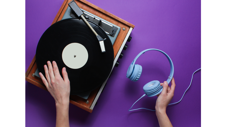 DJ concept. Female hand uses vinyl player and holds the headphones in her hand against a purple background. Retro style. Pop culture. Top view