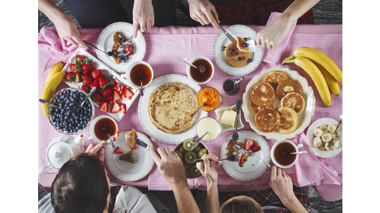 Breakfast table. Flat lay of eating peoples hands over breakfast table with crepes, pancakes, tea and berries.