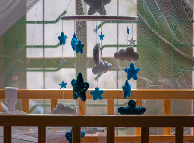 Cot mobile over the babies small bed has purple net over and the baby crib is near the window close up side view,