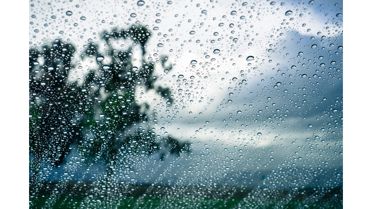 Drops of rain on the window; blurred trees and storm clouds in the background