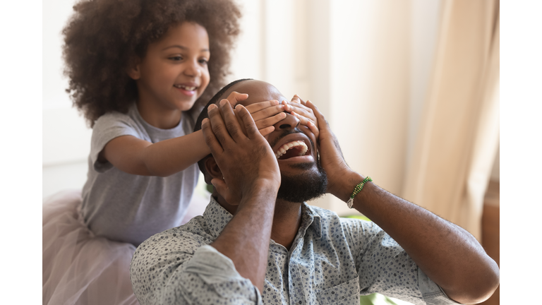 Cute african kid daughter close eyes making surprise for daddy