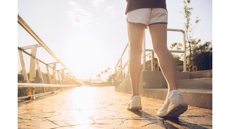 Cropped shot of runner woman running on the way in the park during sunset.