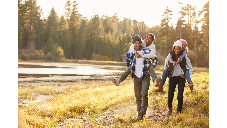 Parents Giving Children Piggyback Ride On Walk By Lake