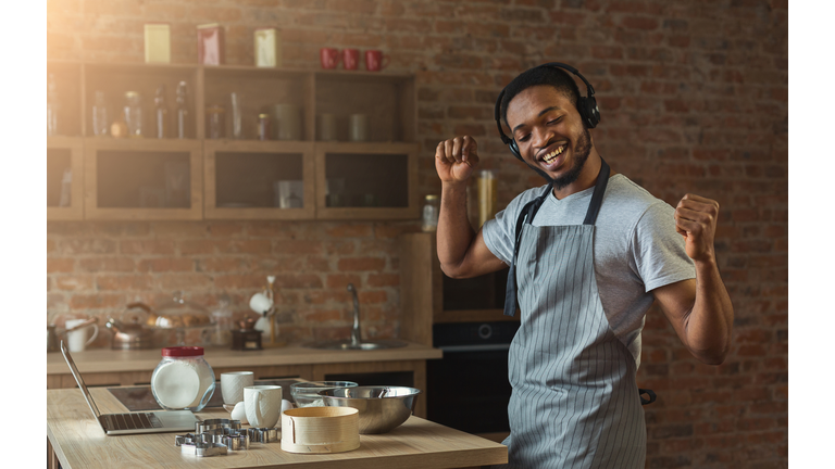 Happy black man listening to music and dancing in kitchen