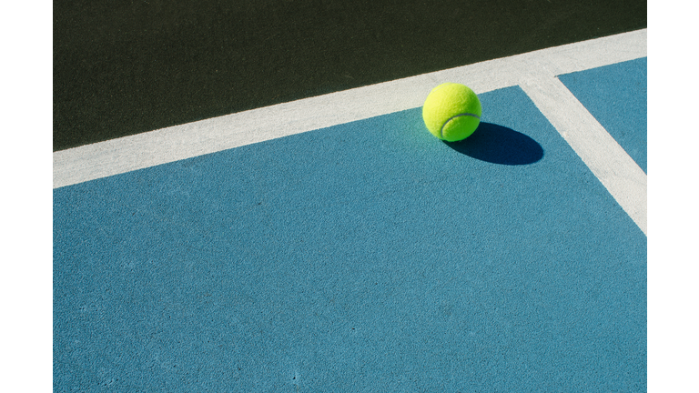 Tennis ball rests on blue tennis court