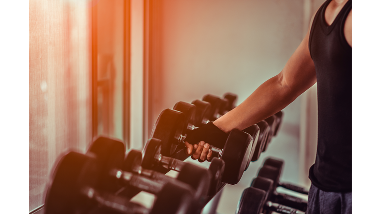 Close up many metal dumbbells on rack in gym.Athlete in the gym training with dumbbells. Hands with dumbbells.