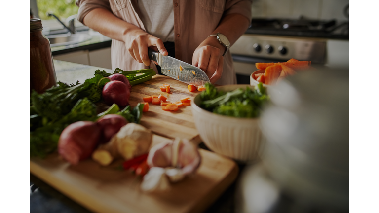 Closeup of young female hands chopping fresh vegetables on chopping board while in modern kitchen - preparing a healthy meal to boost immune system and fight off coronavirus