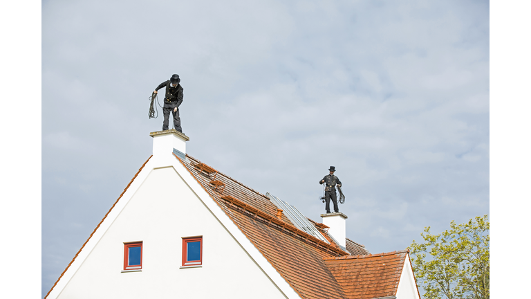 Two chimney sweeps working on house roof