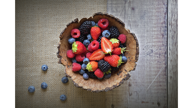 Close-up image of a wooden bowl full of Healthy Summer berries including Strawberries, raspberries, black berries and blue berries.