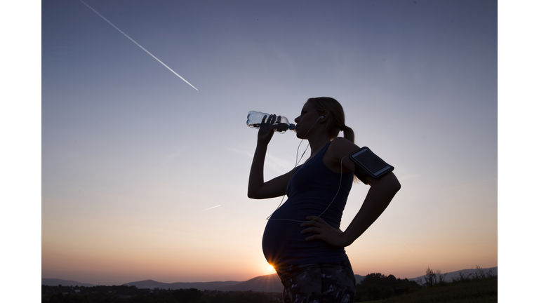 Silhouette of pregnant woman drinking water from bottle at sunset