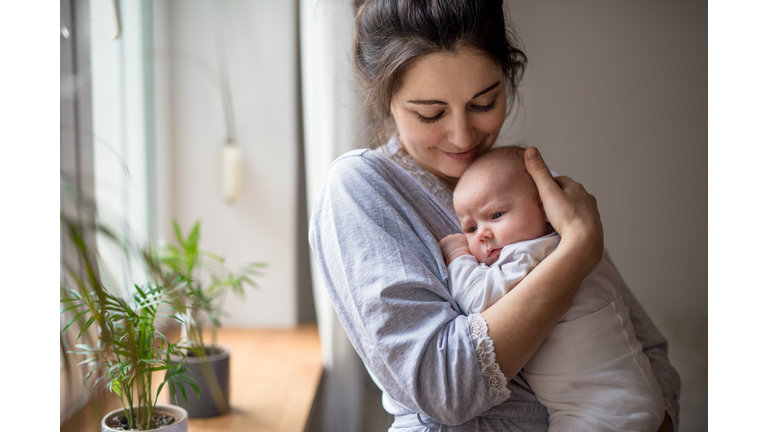 Loving and affectionate mother holding newborn baby indoors at home.