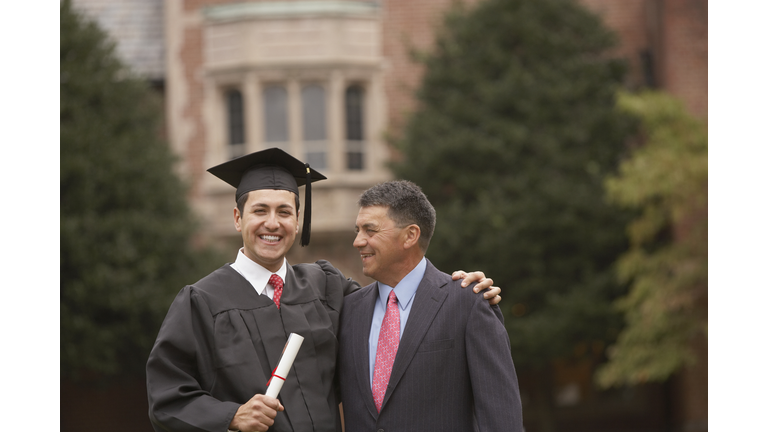 Portrait male graduate in cap and gown with diploma with father