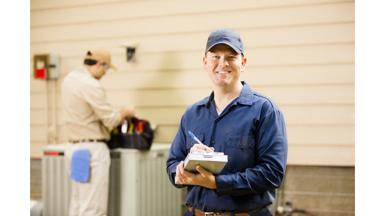 Air conditioner repairmen work on home unit. Blue collar workers.
