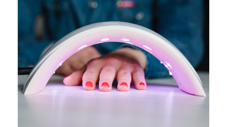 UV lamp with light for drying nails with gel polish. Woman hand inside lamp for nails on table close up. Red nails dried in the lamp. Girl makes a manicure at home, doing manicure herself, draws.