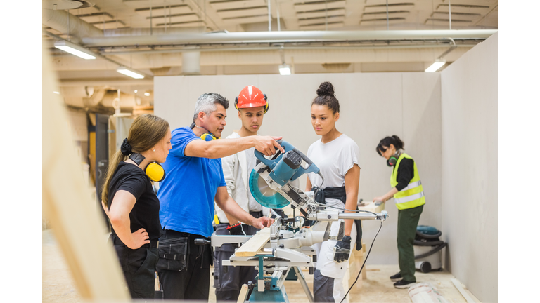 Trainees watching confident male carpenter cutting with electric saw in workshop