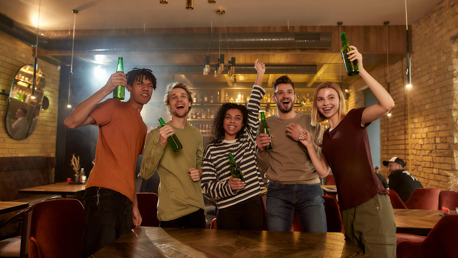 Loud and Proud. Happy friends standing in the bar watching sports match on TV together, drinking beer and celebrating victory. People, leisure, friendship and entertainment concept