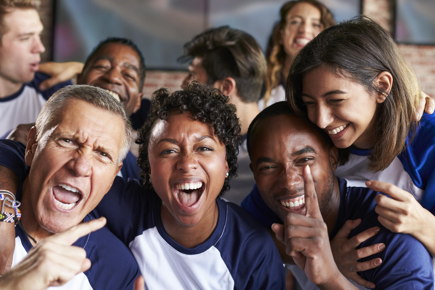 Portrait Of Friends Watching Game In Sports Bar On Screens