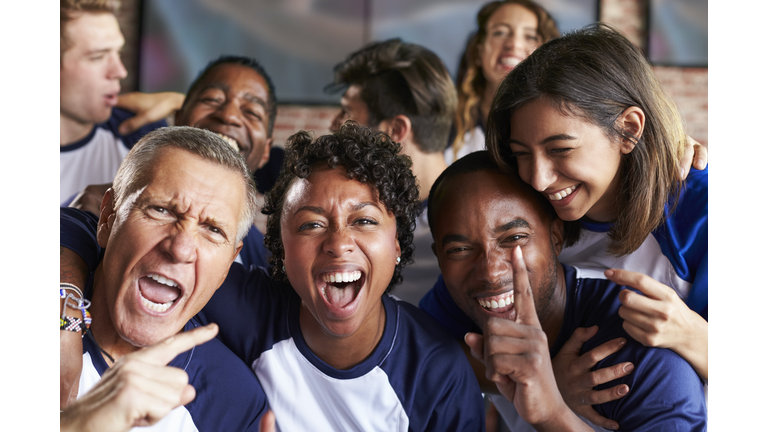 Portrait Of Friends Watching Game In Sports Bar On Screens