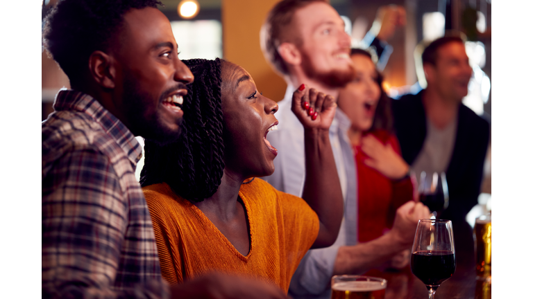 Group Of Excited Customers In Sports Bar Watching Sporting Event On Television