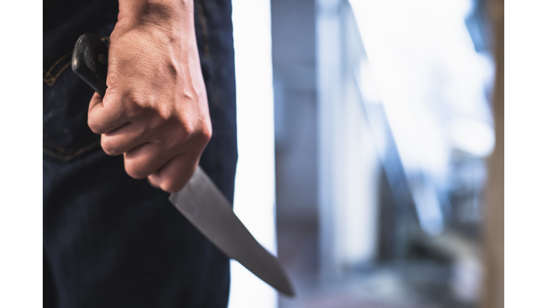 image of a robbers hands holding a knife in the shadows.